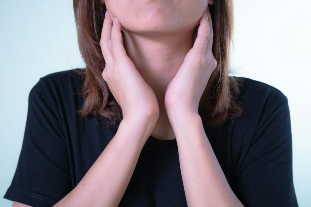 Close-up of a person in a black shirt cupping their neck with both hands, suggesting neck or throat discomfort.